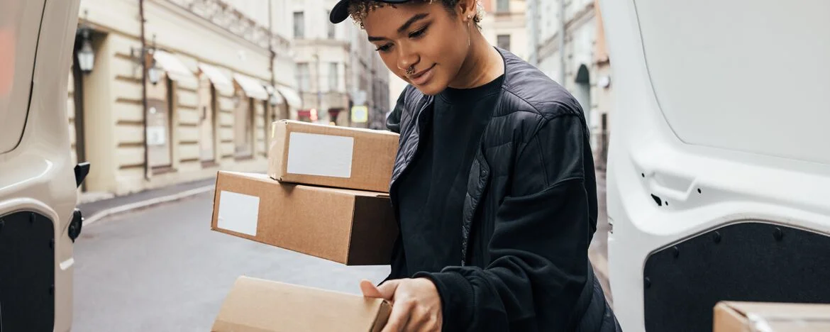 Woman unloading boxes from rear of small white van