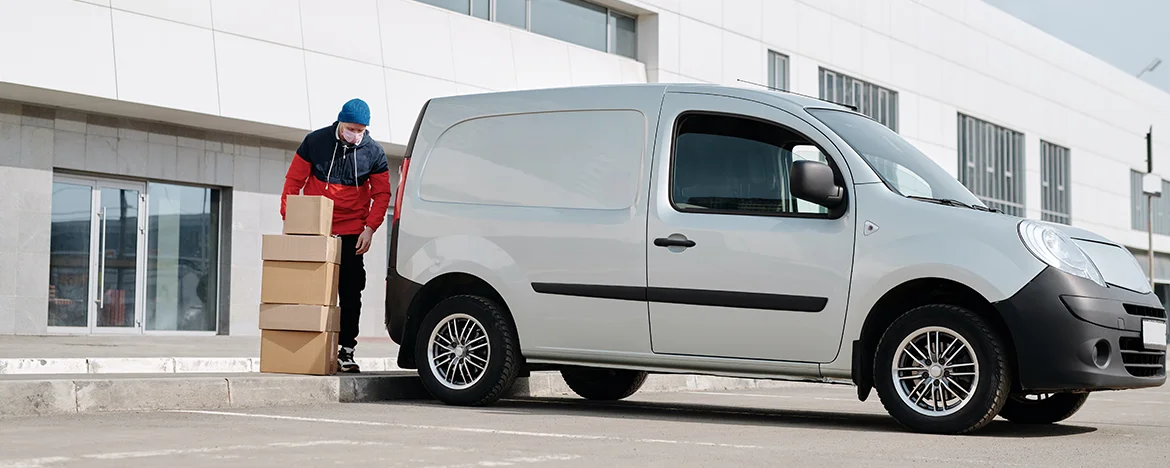 Man in a face mask unloading small panel van of boxes